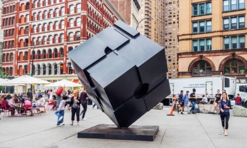 Black cube sculpture in urban plaza setting.