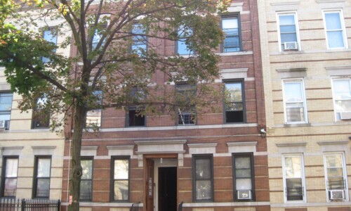 Brick apartment building with tree in front.